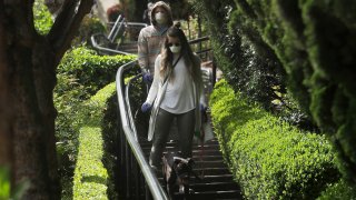 C.J. Pendergast, top, and his girlfriend Krislyn Engelke wear masks and gloves while walking their dog Semi down Lombard Street in San Francisco, Saturday, March 21, 2020. Some 40 million Californians are coping with their first weekend under a statewide order requiring them to stay at home to help curb the spread of the coronavirus.(AP Photo/Jeff Chiu)