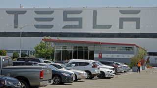 A masked man walks in the Tesla plant parking lot Monday, May 11, 2020, in Fremont, Calif.