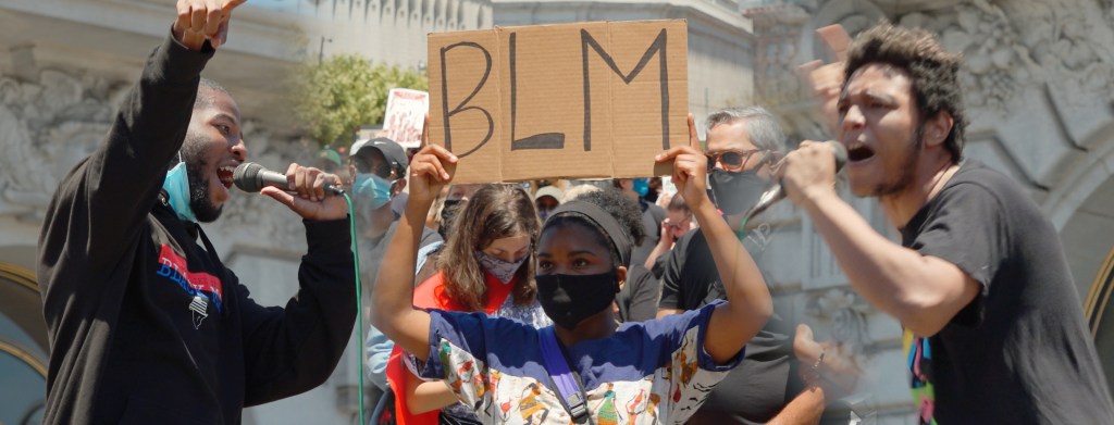 Photo montage with two rappers performing with microphones on the left and right sides, and a young woman holding up a "BLM" sign in the middle.