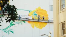 painters working on a giant butterfly mural wave from a scaffold high above the street
