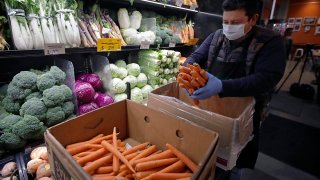 A worker wearing a protective mask stocks produce before the opening of Gus's Community Market, March 27, 2020, in San Francisco.