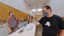 a man uses an iPhone to pay a clerk at a coffee shop. Both are wearing masks over their lower faces.