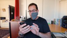 a man wearing a mask looks at an iphone and touches it with his index finger
