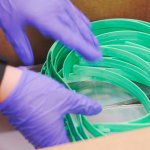 gloved hands place a pile of green plastic headbands into a cardboard box