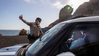 California State Parks ranger David Gunn, left, warns visitors to Pt. Mugu that parking is not allowed due to coronavirus and social distancing restrictions on Saturday, April 11, 2020 in Point Mugu, CA.