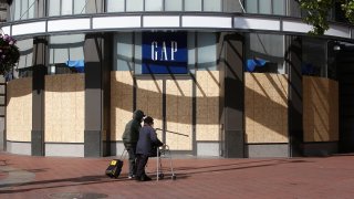 Pedestrians wearing masks walk past a boarded up Gap store