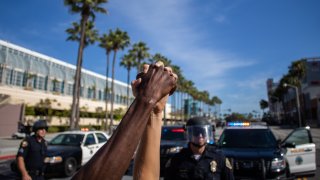 A black man and a white woman hold their hands up in a front of police officers in downtown Long Beach, California