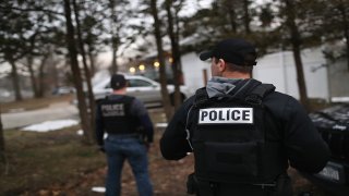 In this March 29, 2018, file photo, Customs and Border Protection officers watch a house as Homeland Security Investigations (HSI) ICE agents detain a suspected MS-13 gang member and Honduran immigrant at his home in Brentwood, New York.