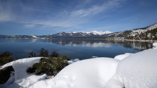 Snow covers the Sierra Nevada mountains and the shoreline of Lake Tahoe