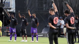 Orlando City players, left, raise their fists in the air in solidarity with other MLS teams before the start of an MLS soccer match, Wednesday, July 8, 2020, in Kissimmee, Fla., while wearing shirts and masks with messages about race.