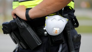 In this March 16, 2020, photo a North Charleston police officer carries a protective mask around his gun belt while working traffic at Roper St. Francis' North Charleston office in North Charleston, S.C.