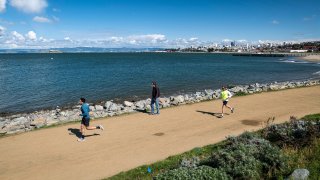 Joggers run past a pedestrian on a trail at Crissy Field in San Francisco.