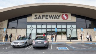 Customers, some wearing protective masks and gloves, wait in a line outside a a Safeway store.