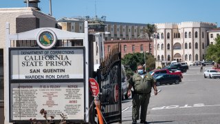 A California Department of Corrections and Rehabilitation (CDCR) officer wearing a protective mask stands at the front gate of San Quentin State Prison.