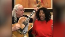 a man with a guitar sits next to a woman singing in a red sweater.