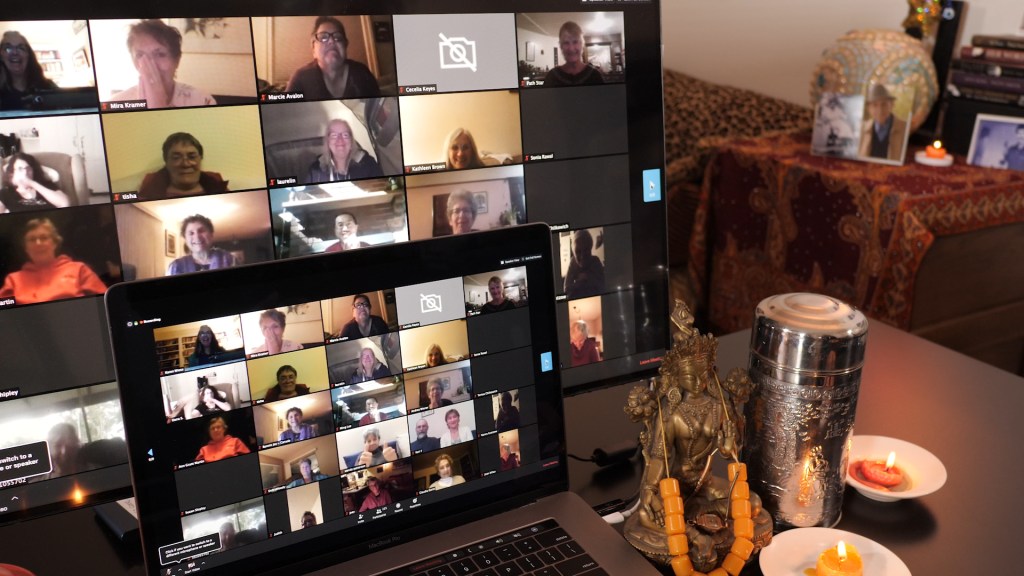 computer sits amid candles and meditation beads with a zoom video conference on the screen