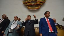 CORRECTS TO REMOVE PARTY AFFILIATION - Lawmaker Luis Parra addresses lawmakers using a megaphone and holding up a miniature copy of Venezuela's constitution, after he was sworn-in as National Assembly president while opposition lawmakers, including opposition Assembly President Juan Guaidó, are blocked by police from entering the session to participate in the vote for new leadership, in Caracas, Venezuela, Sunday, Jan. 5, 2020. Without a quorum, there was no vote for Parra, while the opposition, who enjoy a comfortable majority, immediately denounced the impromptu session as invalid. (AP Photo/Matias Delacroix)