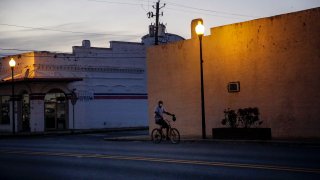 In this April 17, 2020, file photo, a man rides a bicycle down an empty street in Dawson, Georgia.
