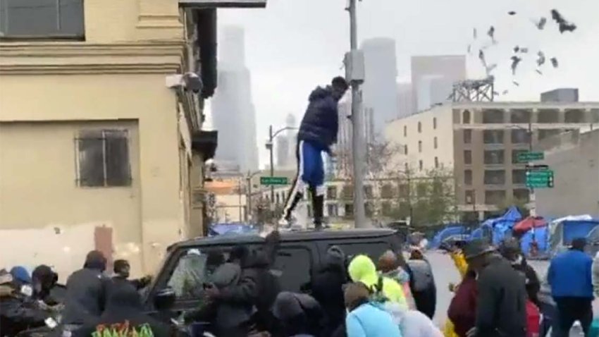Rapper Blueface hurls cash from atop a SUV on LA’s Skid Row.