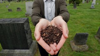 FILE – In this April 19, 2019, file photo, Katrina Spade, the founder and CEO of Recompose, a company that hopes to use composting as an alternative to burying or cremating human remains, poses for a photo in a cemetery in Seattle, as she displays a sample of compost material left from the decomposition of a cow using a combination of wood chips, alfalfa and straw. (AP Photo/Elaine Thompson, File)