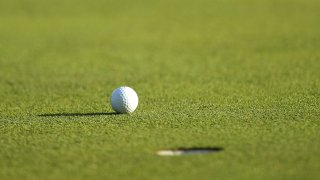 A golf ball is seen resting near a hole.