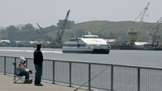 Two men fish along the waterfront as the Vallejo ferry passes with the Mare Island shipyard in the background in Vallejo, Calif., Tuesday, May 6, 2008.