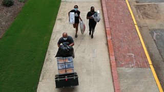 In this July 31, 2020, file photo, a family carries their belongings while college students begin moving in for the fall semester at N.C. State University in Raleigh, N.C.