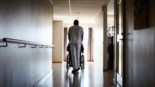 Worker pushing patient in wheelchair in nursing home