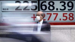 In this July 13, 2020, file photo, a man wearing a face mask to help curb the spread of the coronavirus stands near an electronic stock board showing Japan's Nikkei 225 index at a securities firm in Tokyo.