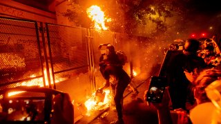 Protesters throw flaming debris over a fence at the Mark O. Hatfield United States Courthouse on Wednesday, July 22, 2020, in Portland, Ore.