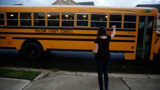 Rachel Adamus waves goodbye to her two children, Paul and Neva, as they ride the bus for the first day of school on Monday, Aug. 3, 2020, in Dallas, Ga.
