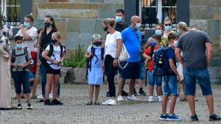 FILE - In this Wednesday, Aug. 12, 2020 file photo, parents wait with children on the schoolyard for the start of their first day at a school in Gelsenkirchen, Germany. Just in time for back-to-school for millions of kids, the World Health Organization on Monday, Aug. 24, 2020 has issued guidance about mask-wearing by children, suggesting in particular that those aged 6 to 11 should wear them too in some cases to help fight the spread of the coronavirus. The WHO recommendations follow upon the widespread belief that children aged under 12 are not considered as likely to propagate the virus as much as adults.