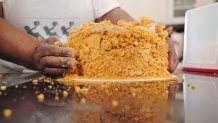 A Black woman's hands apply golden crumbly candy topping to a round cake.