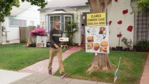 A man leaves a house holding a bakery box with a cake in it. A sign in front of the house reads "Claires Crunch Cake"