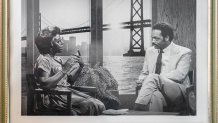 An African-American woman with short hair and glasses intervews the Rev. Jesse Jackson in a television studio against a backdrop that depicts the Bay Bridge