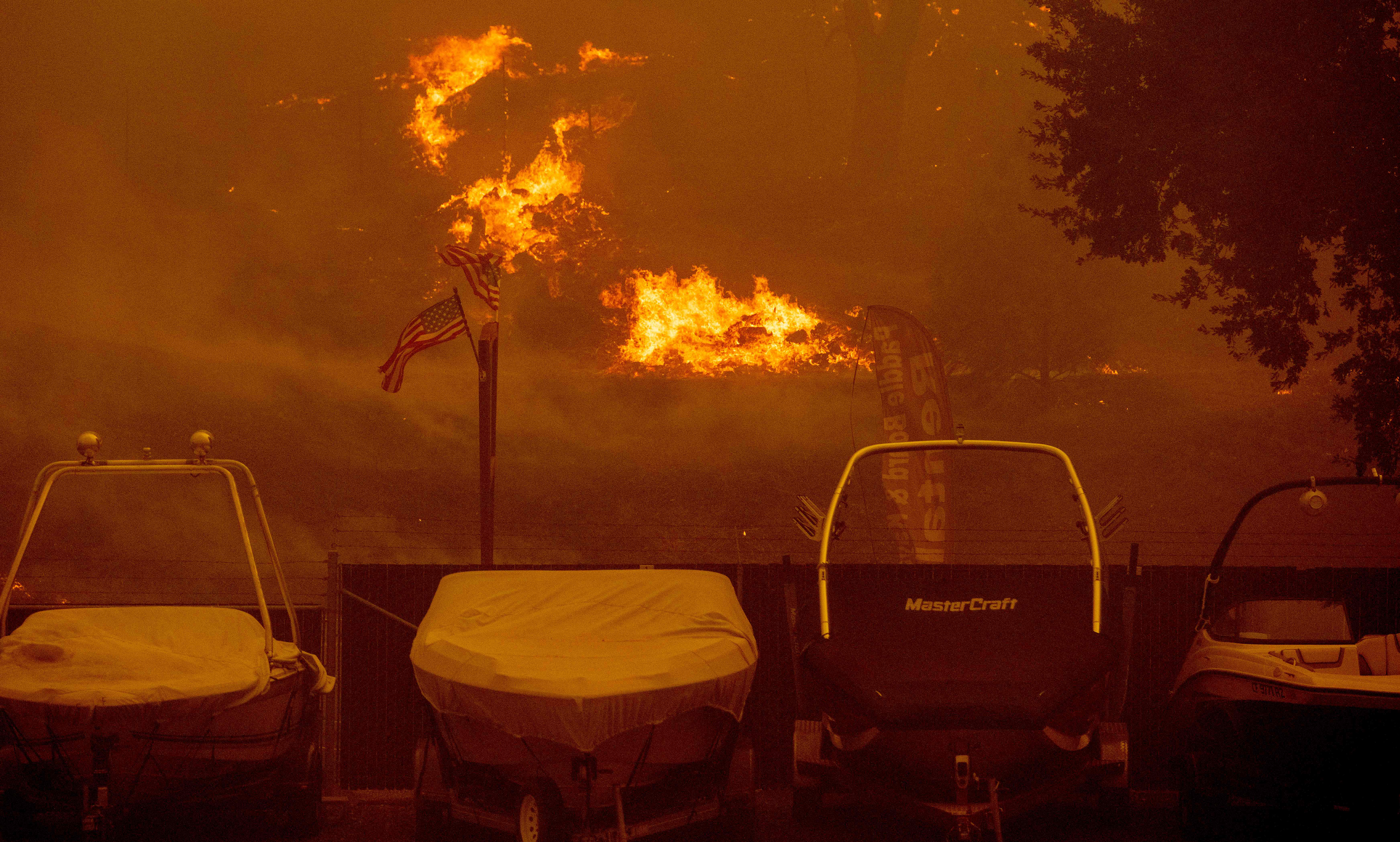 American flags wave in the wind as flames approach a boat rental shop in the Spanish Flat area of Napa, California during the Hennessey fire on August 18, 2020. – As of the late hours of August 18, the Hennessey fire has merged with at least 7 fires and is now called the LNU Lightning Complex fires. Dozens of fires are burning out of control throughout Northern California as fire resources are spread thin. (Photo by JOSH EDELSON / AFP) (Photo by JOSH EDELSON/AFP via Getty Images)