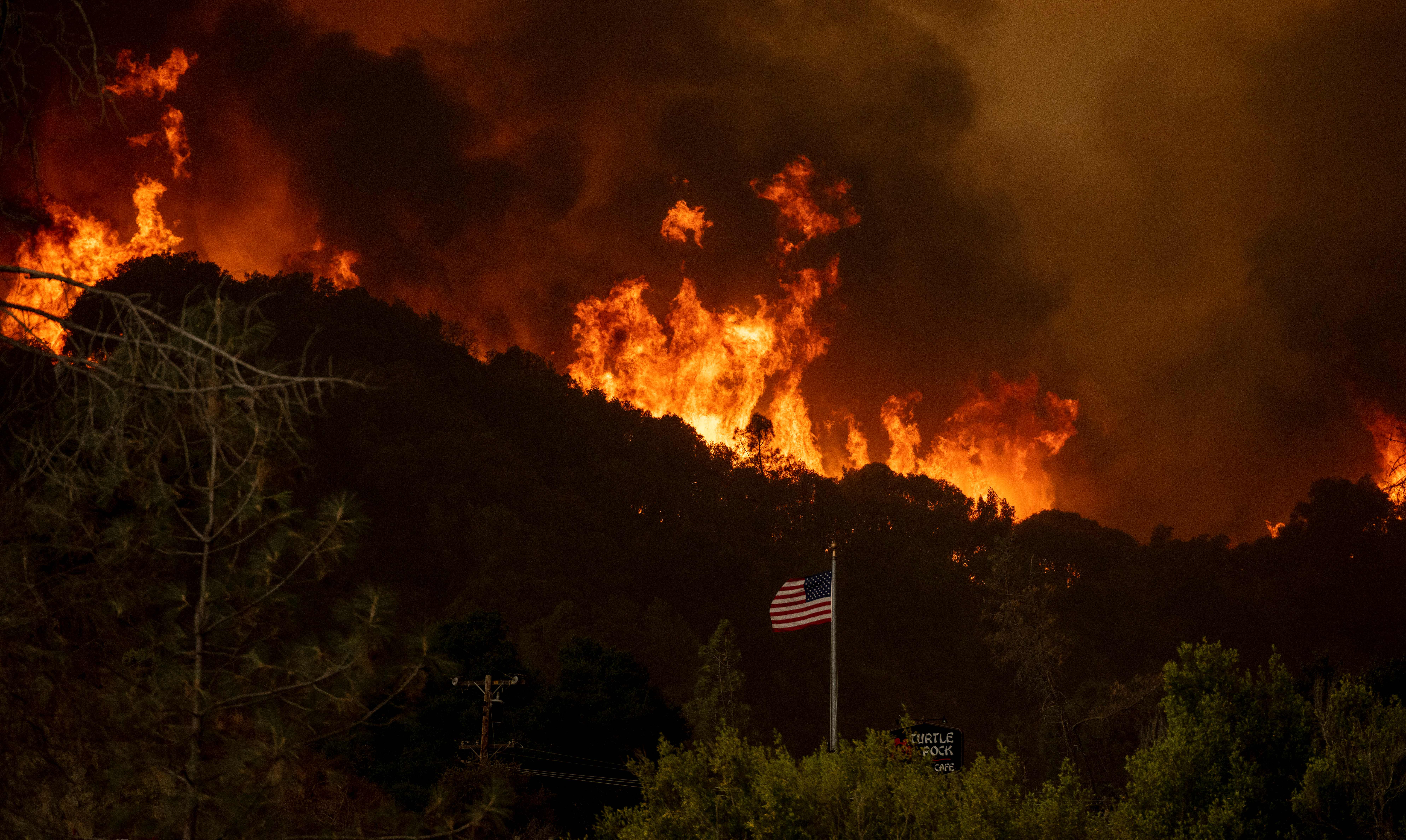 An American flag blows in the wind as flames approach during the Hennessey fire in the Spanish Flat area of Napa, California on August 18, 2020. – As of the late hours of August 18,2020 the Hennessey fire has merged with at least 7 fires and is now called the LNU Lightning Complex fires. Dozens of fires are burning out of control throughout Northern California as fire resources are spread thin. (Photo by JOSH EDELSON / AFP) (Photo by JOSH EDELSON/AFP via Getty Images)