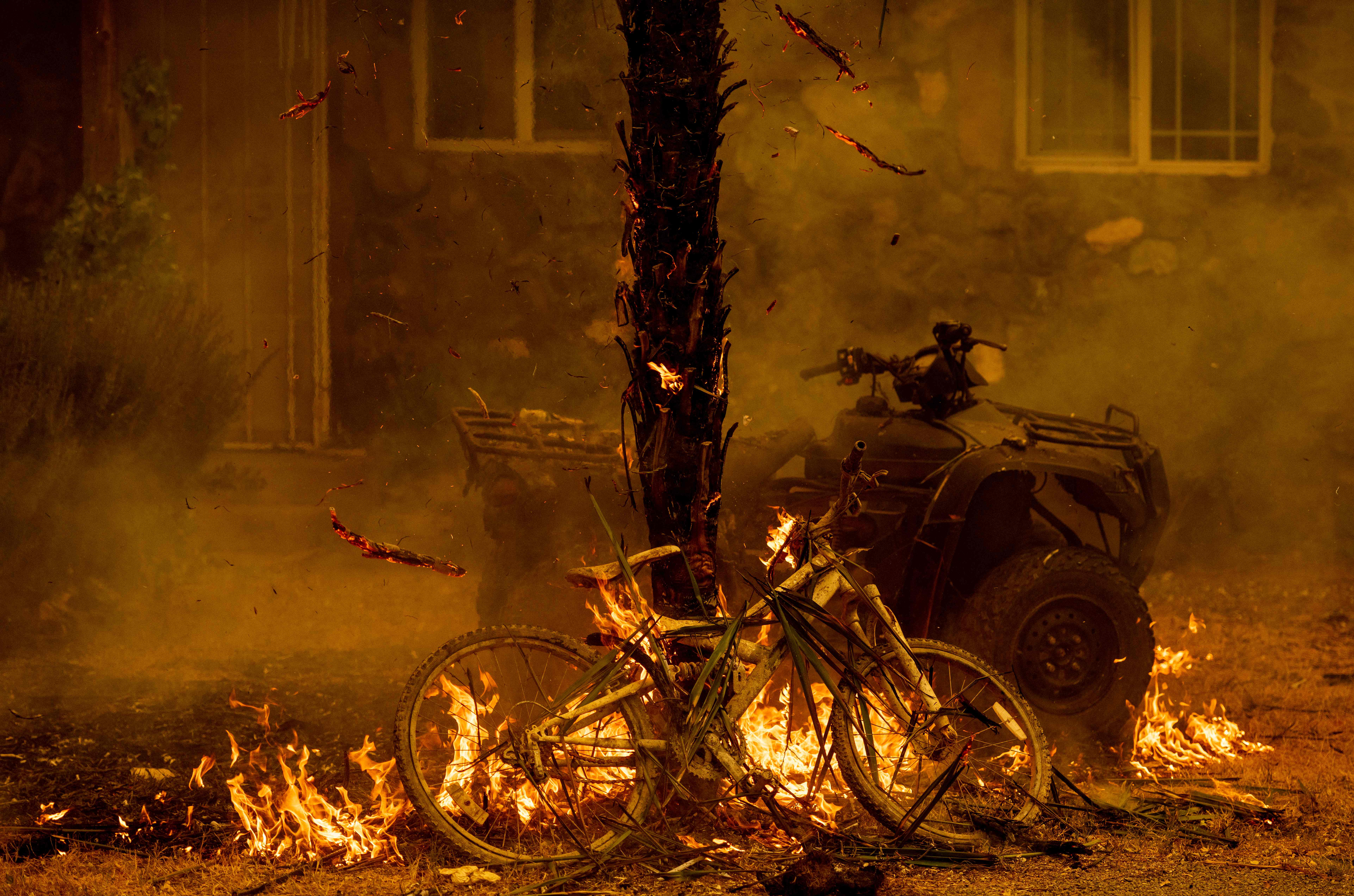 A bicycle and palm tree burn at a residence during the LNU Lightning Complex fire in the Spanish Flat area of Napa, California on August 18, 2020. – As of the late hours of August 18,2020 the Hennessey fire has merged with at least 7 fires and is now called the LNU Lightning Complex fires. Dozens of fires are burning out of control throughout Northern California as fire resources are spread thin. (Photo by JOSH EDELSON / AFP) (Photo by JOSH EDELSON/AFP via Getty Images)