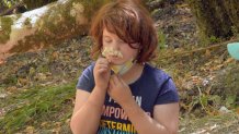 a redheaded girl in a blue T-shirt smells a small handful of white wildflowers