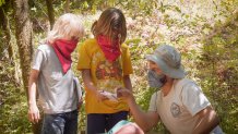 camp instructor talks to two kids wearing red bandanas on their faces.