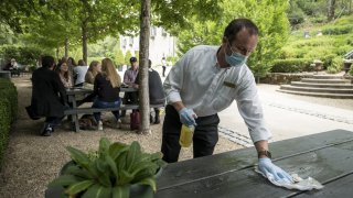 An employee wearing protective gloves and a mask cleans a table at the Buena Vista Winery tasting area in Sonoma.