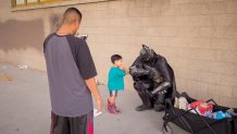 A man dressed as Batman poses for a picture with a small child. They bump elbows.