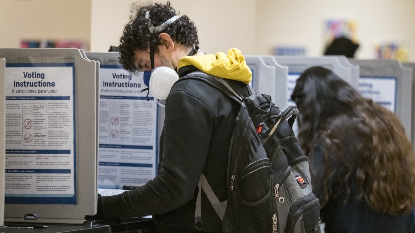 A voter wearing a respiratory mask casts a ballot at a polling station in City Hall in San Francisco, Calif.