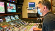 A man wearing a surgical mask sits at an audio mixing board