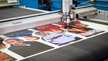 a CNC cutting machine cuts out head-and-shoulders photos from a rectangular batch of 8 printed on a large white board