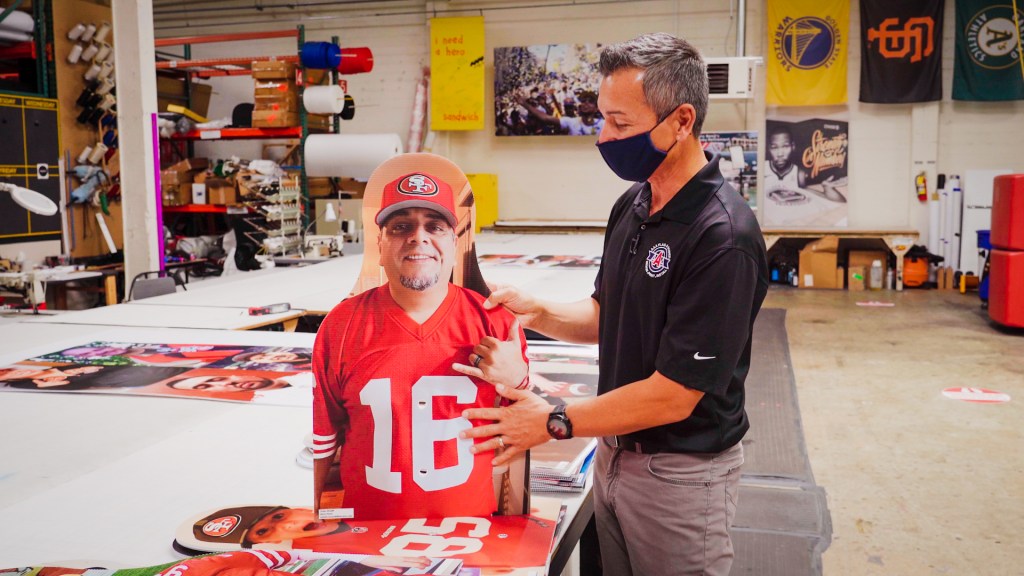 a man in warehouse points out features of a large cut-out 49ers fan photo