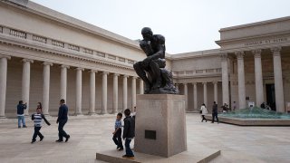 The Thinker, a statue with a man with his hand to his cheek thinking, in the middle of a courtyard.