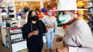 Customer Tamara Jenkins tries on a hat with Meeka Robinson Davis, owner of One-Of-A-Kind Hats, as Davis’ daughter Chrstiana Davis looks on, at the store in the Windsor Hills neighborhood of Los Angeles, California, November 24, 2020.