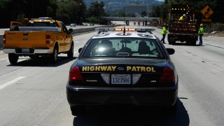 A California Highway Patrol cruiser waits to lead motorist on as construction workers remove barricades.