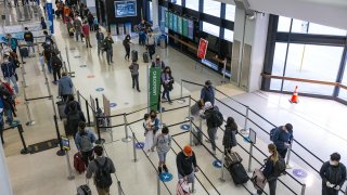 Travelers wearing protective masks wait in line to go through security at San Francisco International Airport (SFO) in San Francisco, California, U.S., on Monday, Nov. 24, 2020. Airlines set a new post-pandemic record for U.S. passengers on Sunday as the Thanksgiving holiday spurred travel despite government warnings.